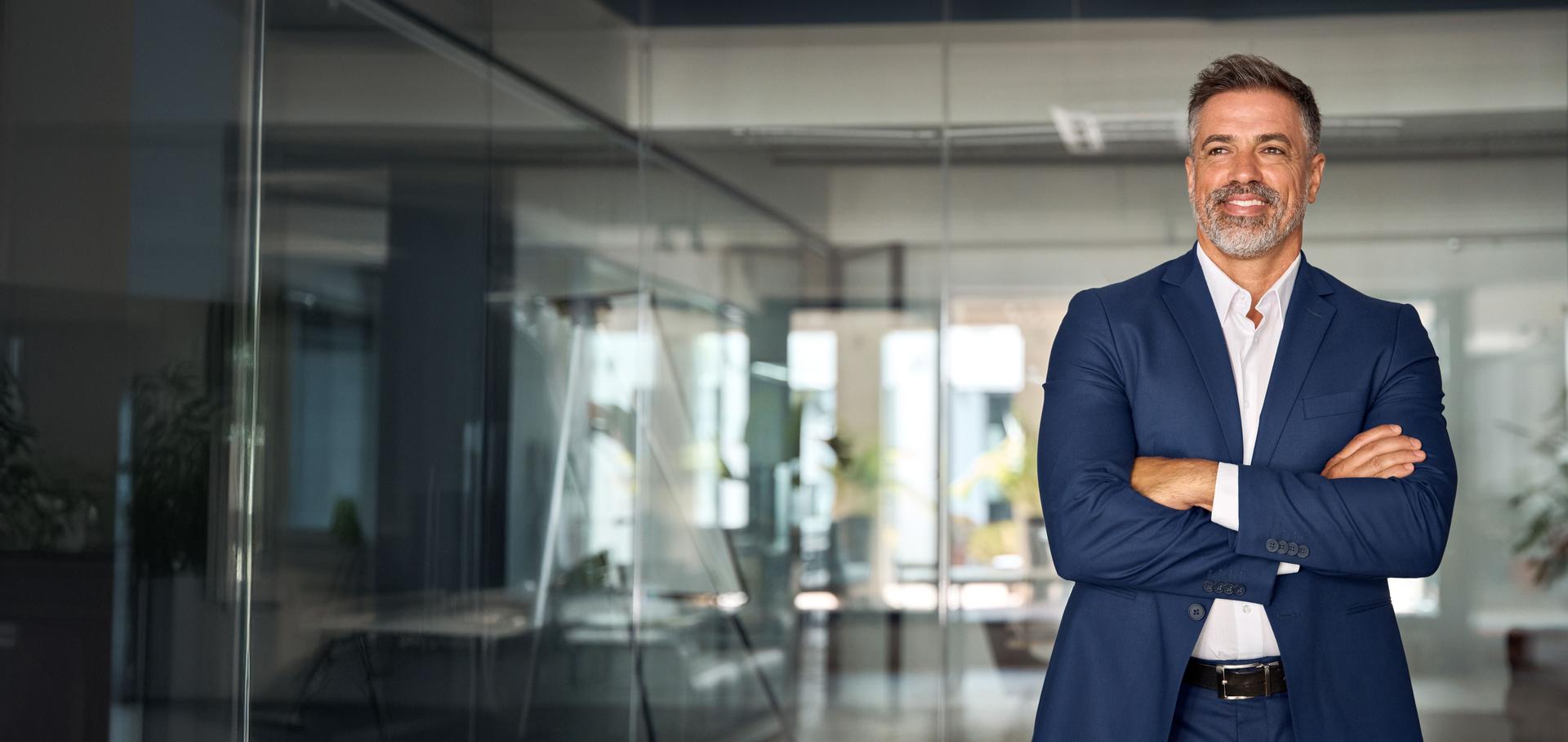Handsome smiling confident hispanic senior man with crossed arms looking aside. Indian or latin successful mature middle age leader male businessman, business investor in office. Banner, copy space.